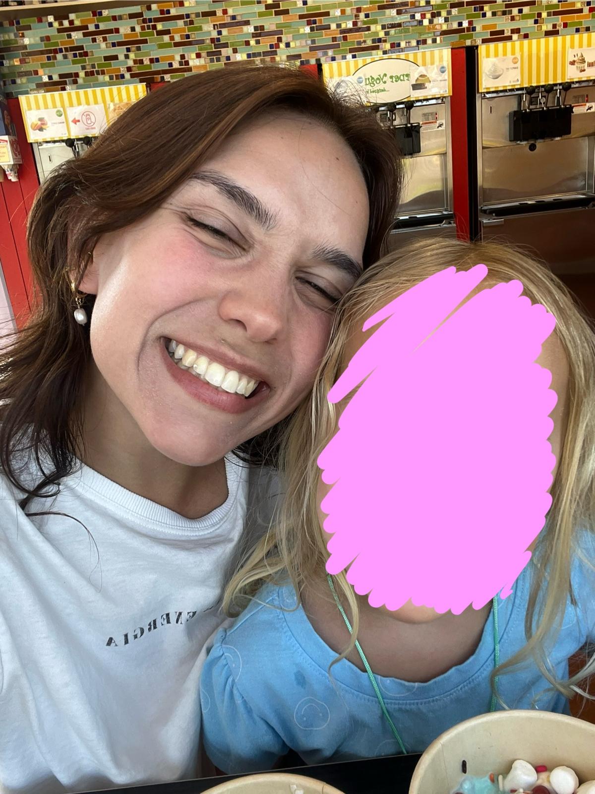 Aurora Carlin Martini cheek to cheek with a child at a frozen-yogurt counter, the child’s face covered by a pink mark.