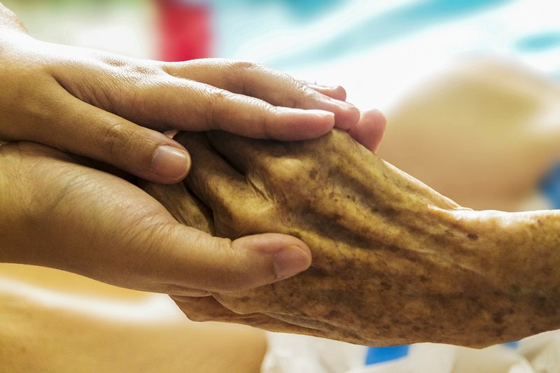 A younger hand cupped around an older, age-spotted hand, photographed close in warm light.