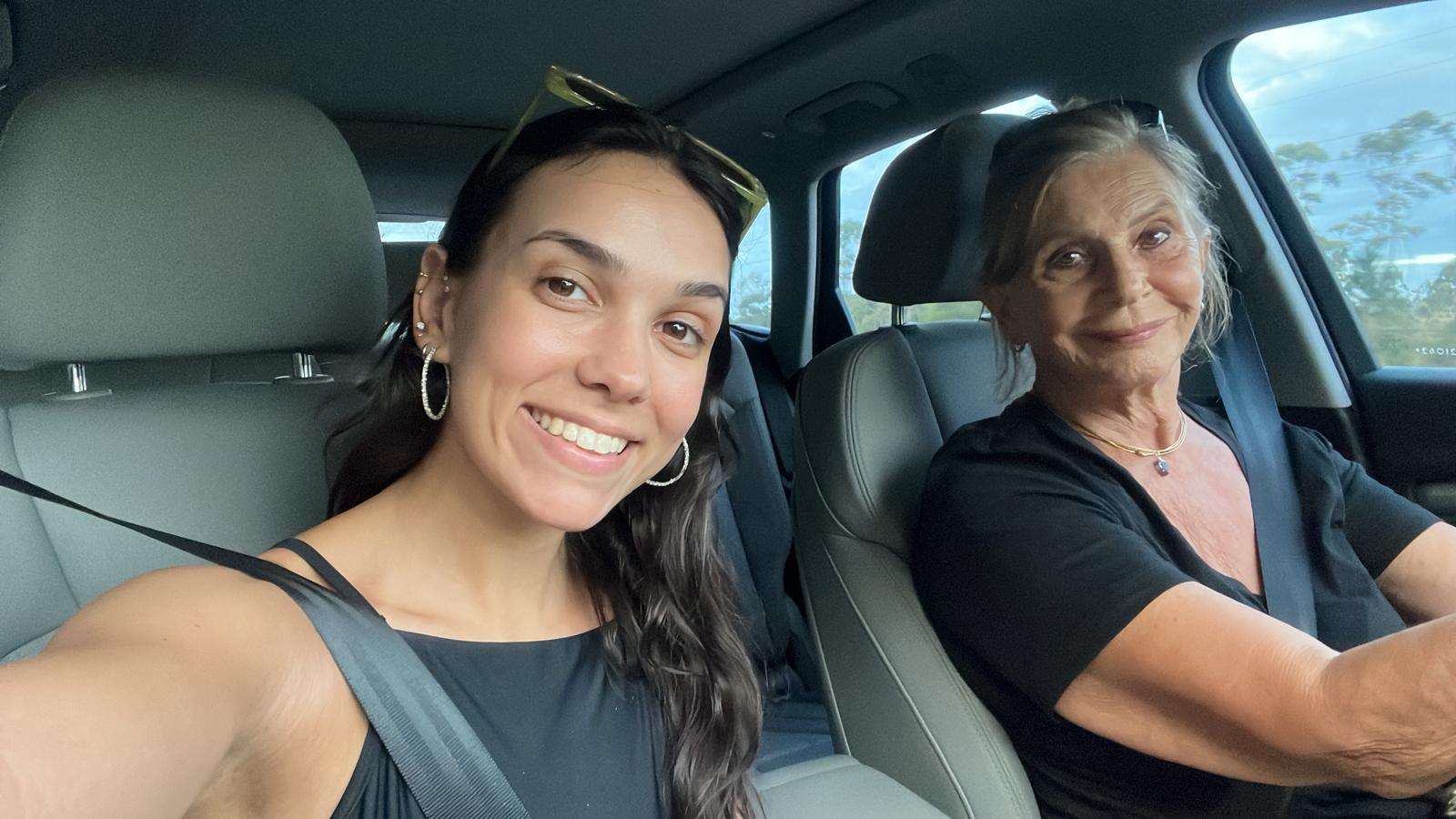 A selfie taken inside a car: Aurora Carlin Martini in the passenger seat and an older woman at the wheel, trees through the windows.