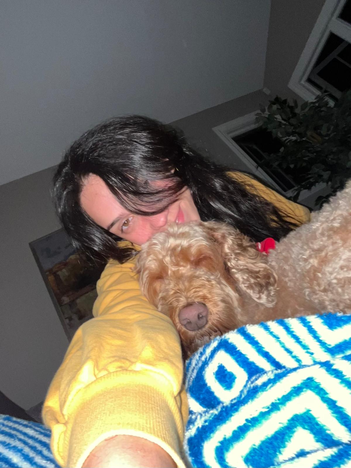 Aurora Carlin Martini indoors at night with a curly apricot-coated dog resting beside her on a patterned blanket.