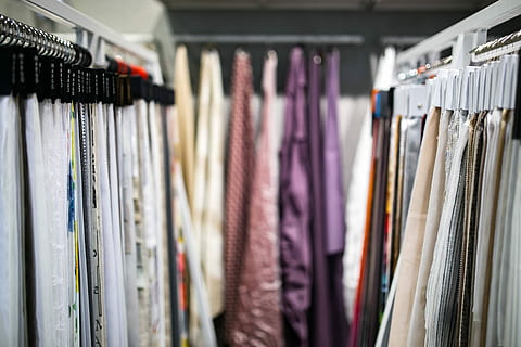 Rows of garments hanging in dry-cleaning plastic along a rail, photographed with a shallow depth of field.