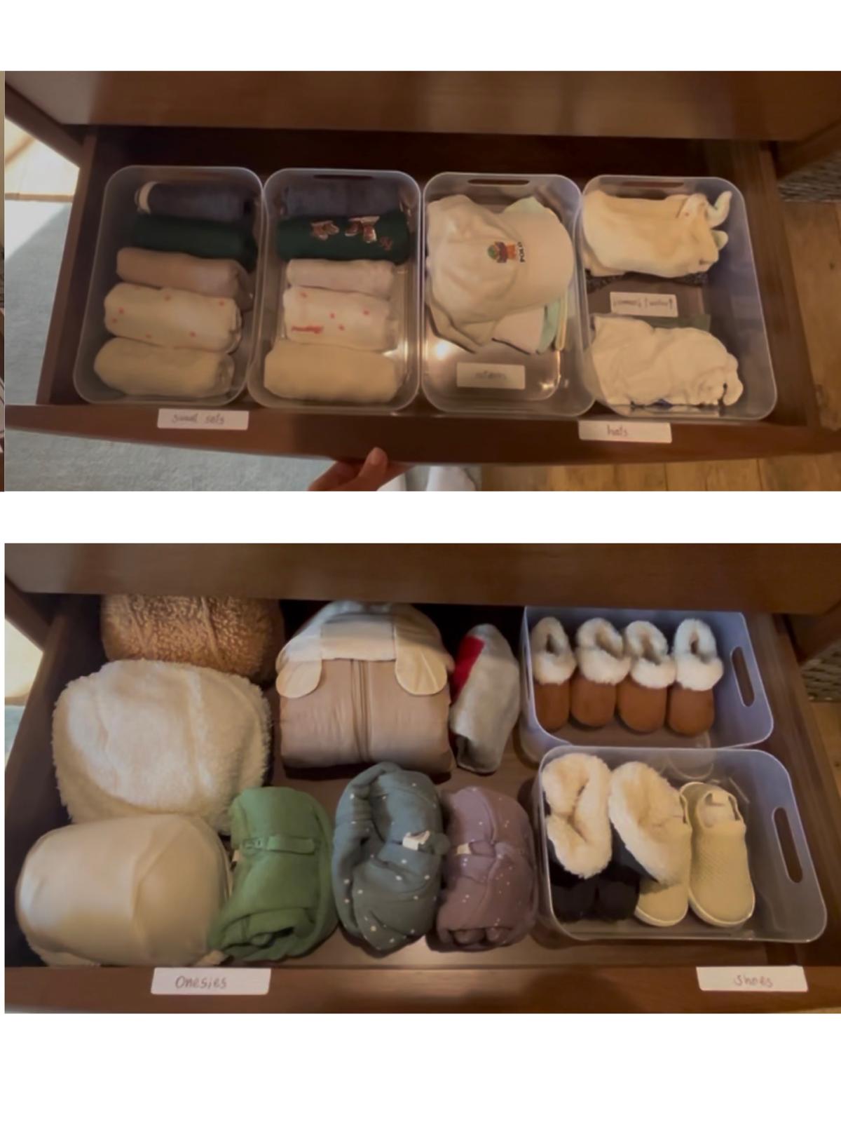 Two open drawers holding clear bins of infant clothing, hats and shoes, each bin fronted by a handwritten label; a hand steadies the upper drawer.